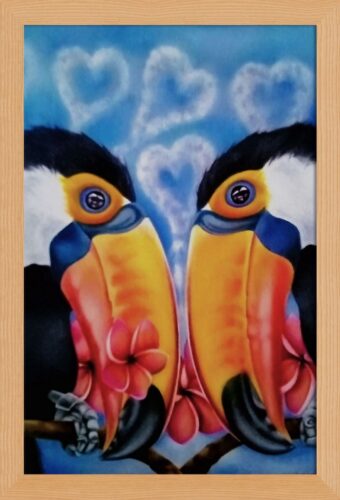 Two toco toucans facing each other, with their beaks in a downward position. In love one of the toucans has a pink flower in its beak, both are perched on a branch with pink flowers behind them. Blue sky background with heart-shaped clouds. Framed painting.